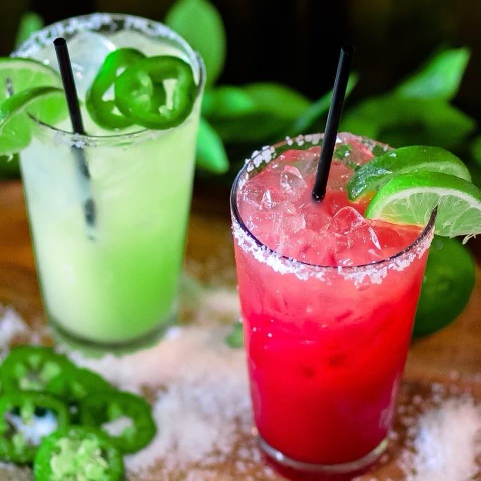 Two colorful cocktails with lime and jalapeño garnishes