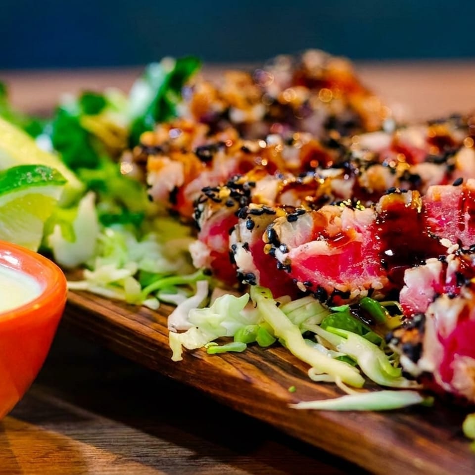 Seared tuna with sesame seeds, sauce, lime wedges, and a side of creamy dip.