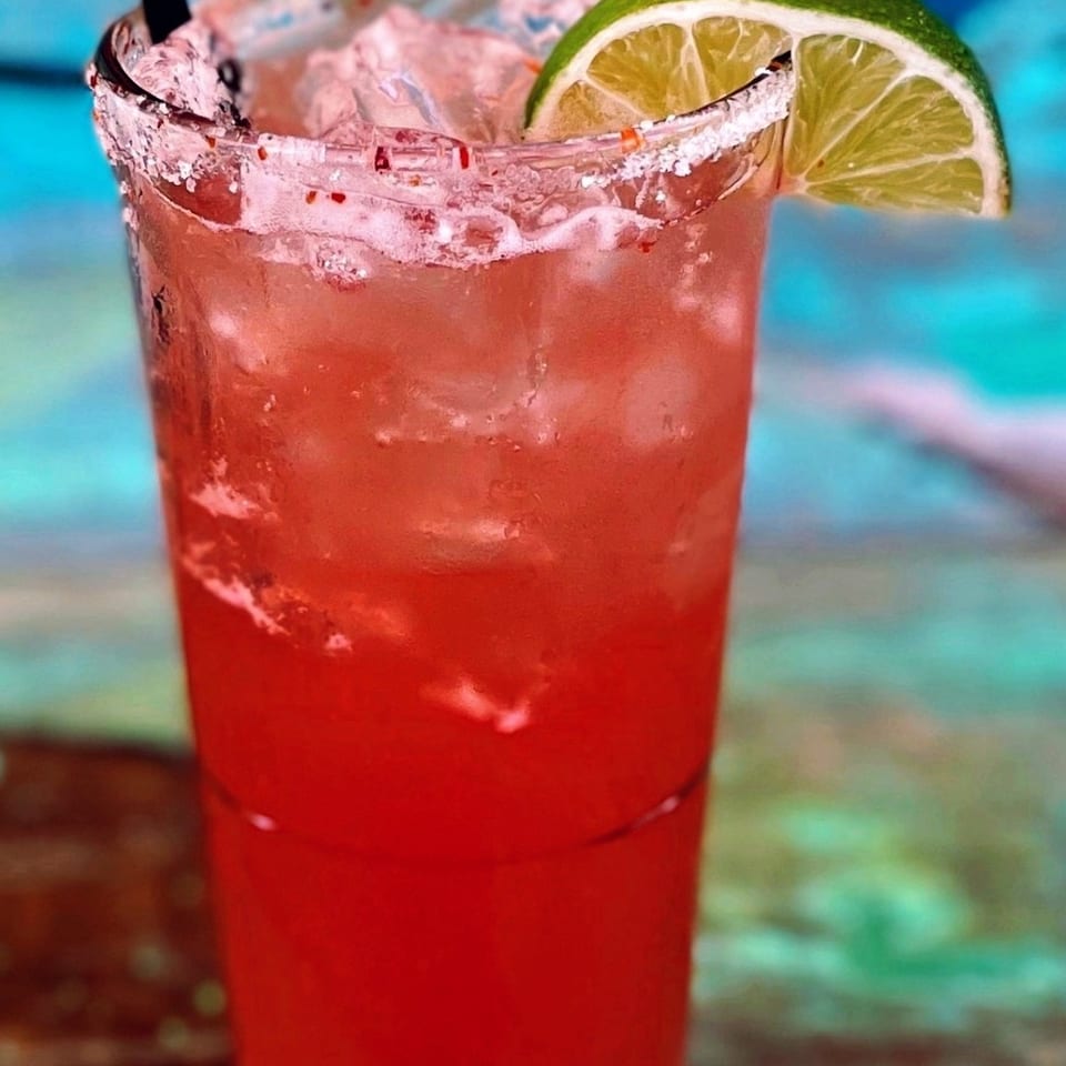 Red cocktail over ice with a lime wedge and seasoned rim