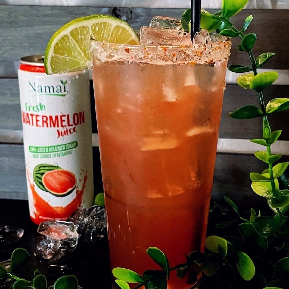 Watermelon-colored cocktail served over ice with lime